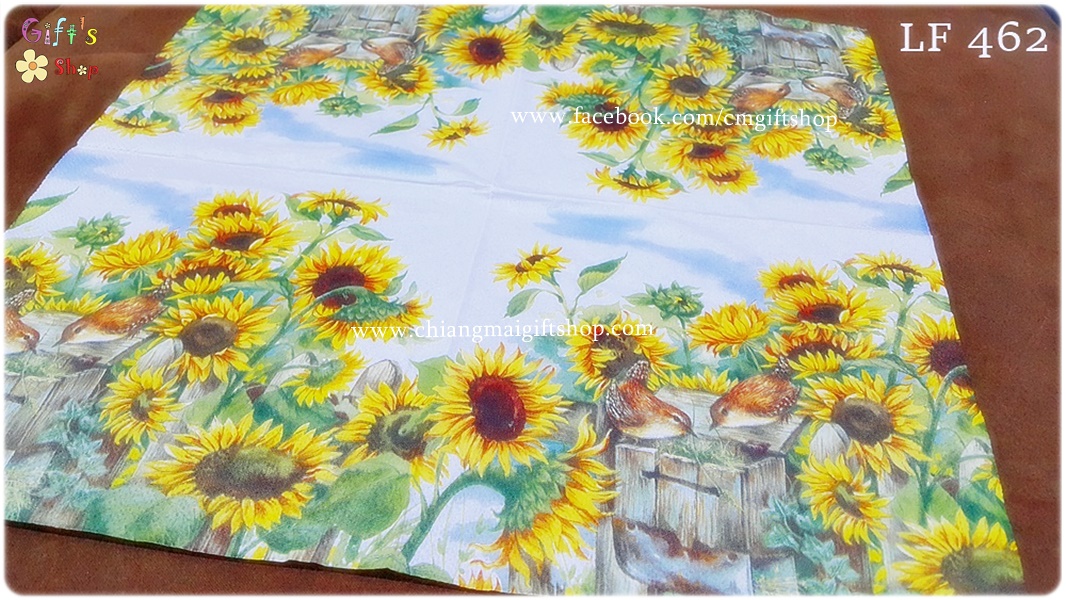 กระดาษแนปกิ้น ลายทุ่งดอกทานตะวันสีเหลืองสดใสใบสีเขียว มีนกสีส้มน้ำตาลกินอาหารนกบนลังไม้ที่ให้อาหารนก พื้นหลังท้องฟ้าและเมฆสีขาว
